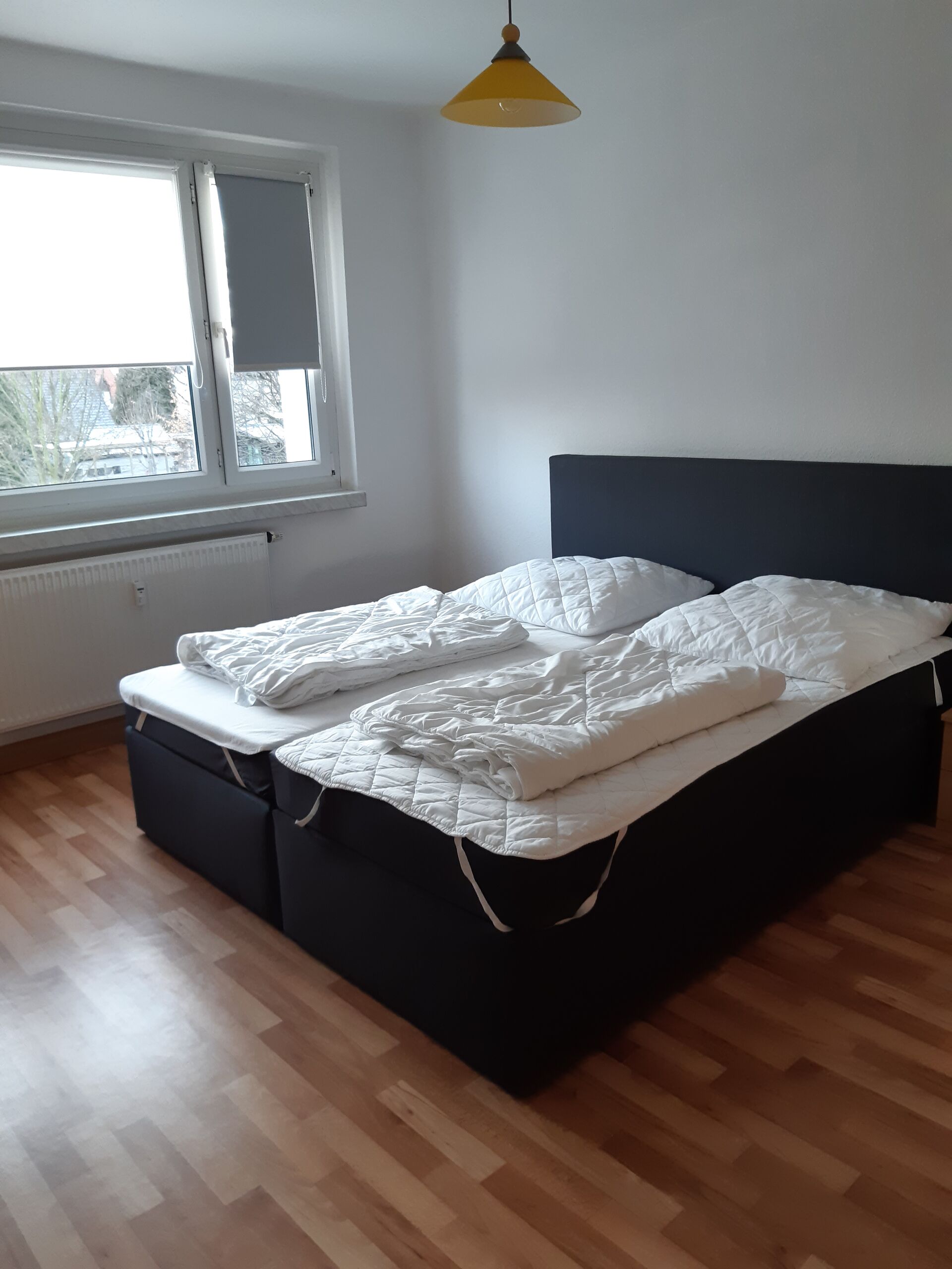Gästewohnung in Gröditz, Am Kanal 27 - Schlafzimmer mit einem schwarzen Bett für zwei, Heizung und Plissees vor dem Fenster