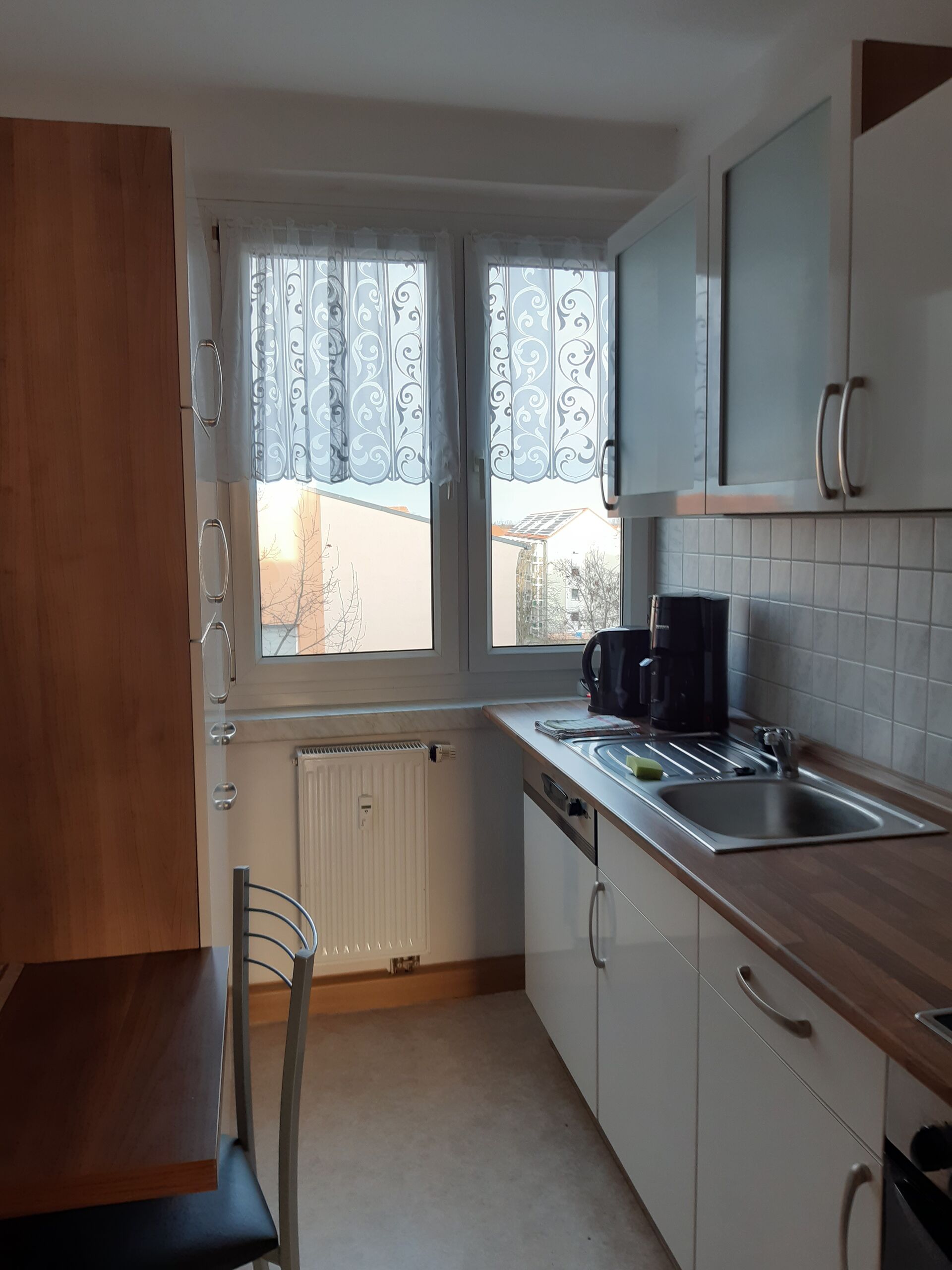 Gästewohnung in Gröditz, Am Kanal 25 - Küche mit einem Esstisch, weiße Schränke, Waschbecken, Kaffeemaschine und Wasserkocher