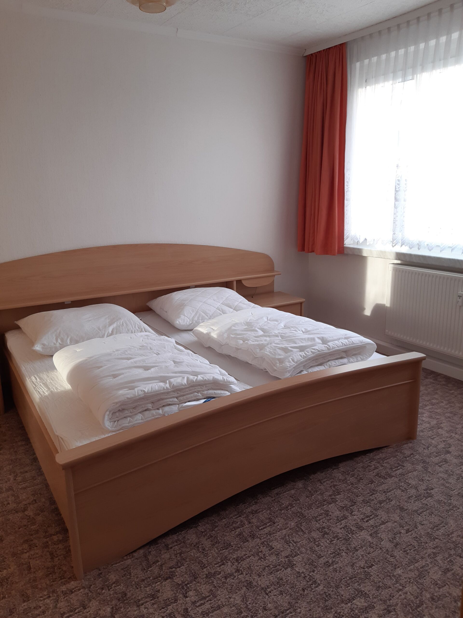 Gästewohnung in Gröditz, Am Kanal 23 - Schlafzimmer mit einem Holzbett, Teppich und roten Gardinen