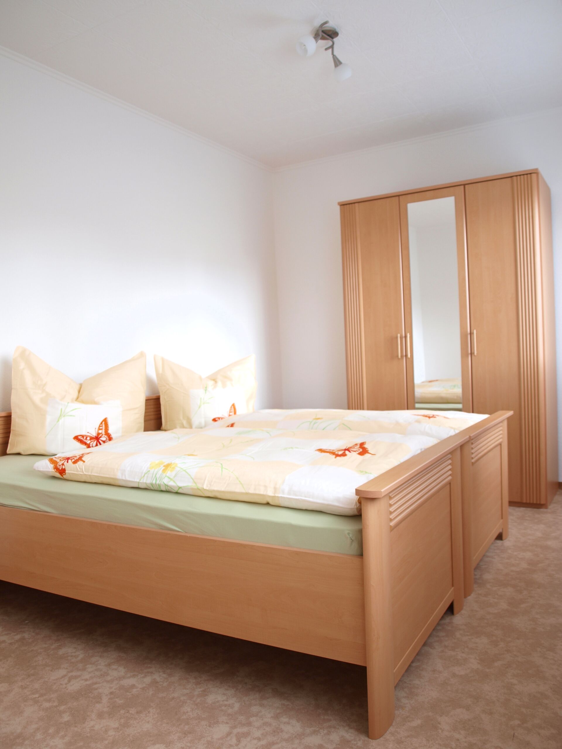 Gästewohnung in Gröditz Mozartallee 11-3 - Schlafzimmer mit Holzbett, orangene Bettwäsche mit Schmetterlingen & Holzschrank mit Spiegel