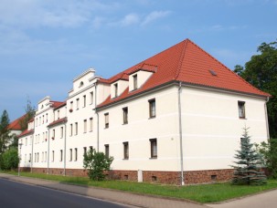 Ein weißes Wohnhaus mit rotem Ziegeldach und grüner Rasenfläche davor in Gröditz. Mietobjekt der KWG.